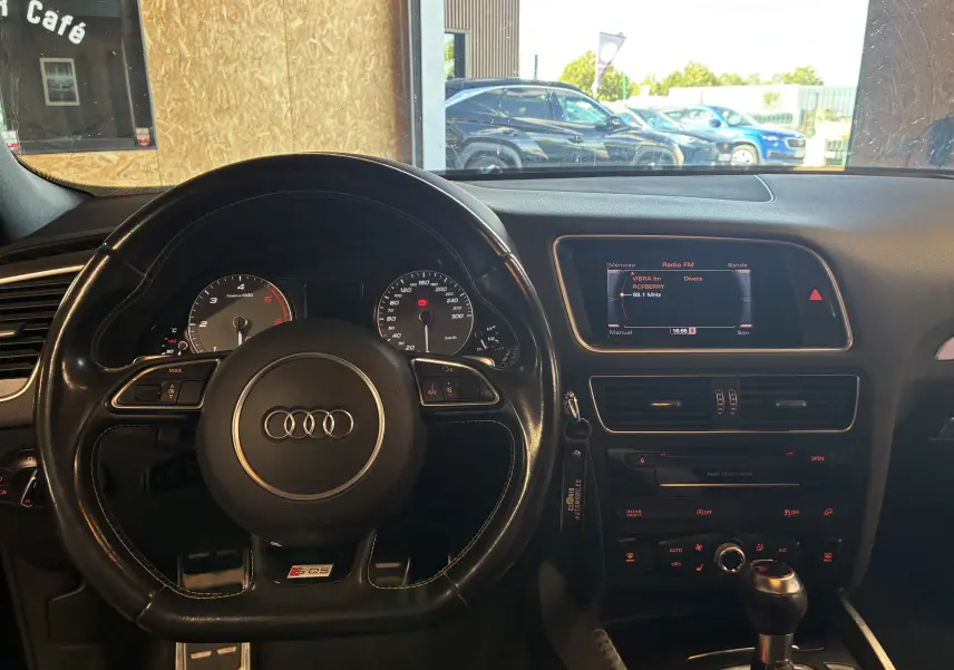 Vue intérieure centrée sur le volant sport Audi SQ5 noir avec tableau de bord et écran multimédia allumé.