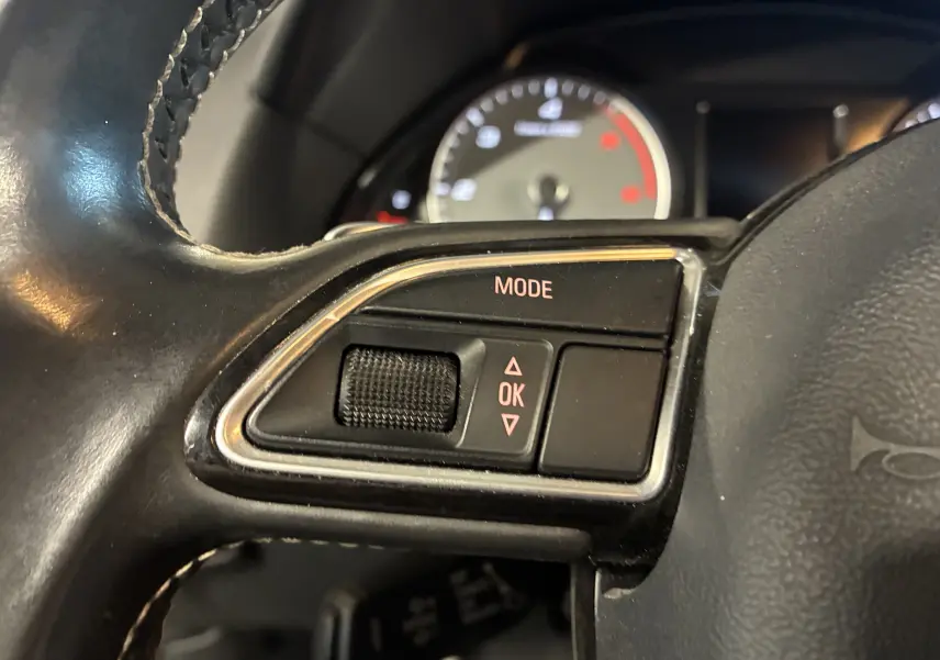 Gros plan sur les commandes mode et OK du volant cuir noir de l'Audi SQ5 2016, avec tableau de bord flou en arrière-plan.