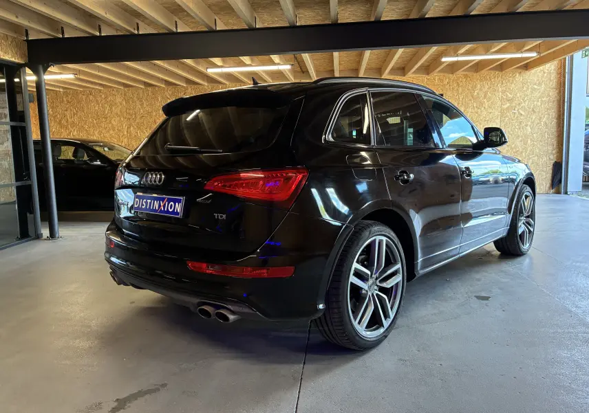 Audi SQ5 noir vue 3/4 arrière droit en intérieur, avec jantes alu et sorties d'échappement chromées visibles.