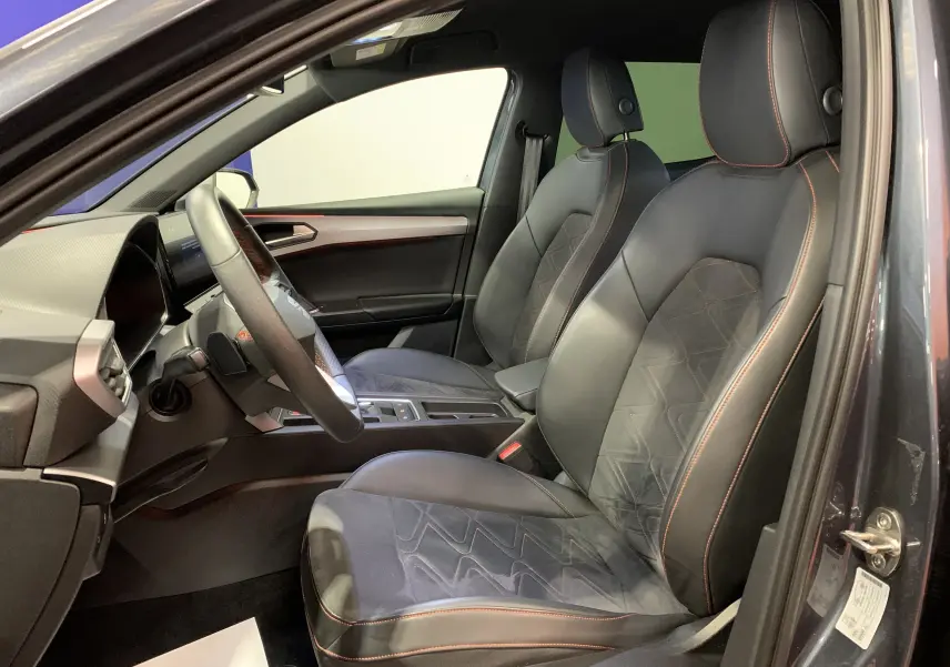 Intérieur côté conducteur d'une SEAT Leon E-HYBRID gris 2020, sièges cuir noir avec surpiqûres rouges et tableau de bord moderne.