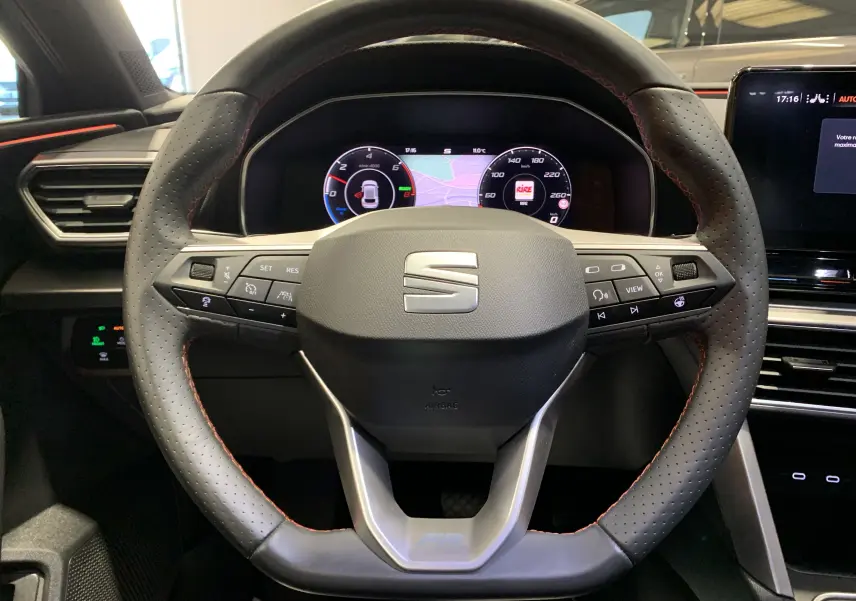 Vue rapprochée du volant perforé noir avec surpiqûres rouges du tableau de bord digital d'une SEAT LEON E-HYBRID 2020.