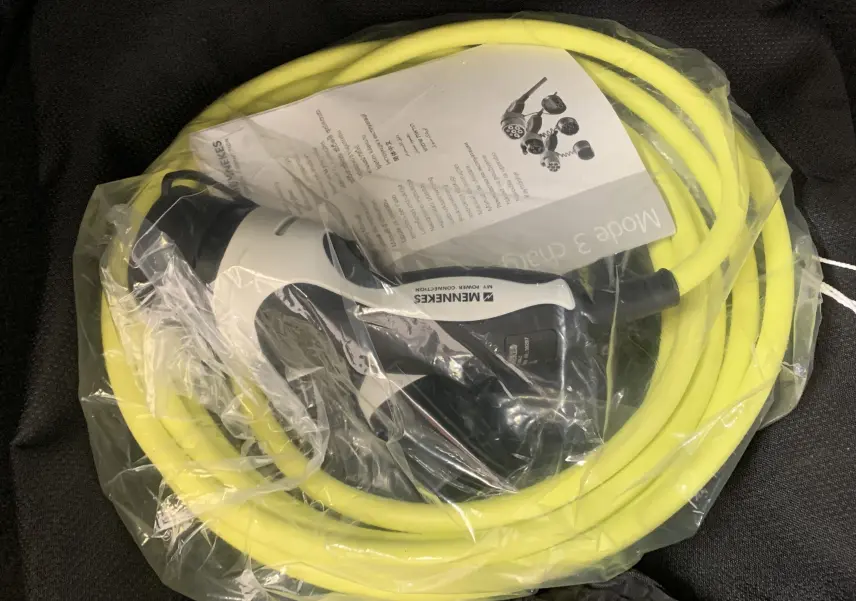Gros plan sur un câble de recharge jaune et sa prise Mennekes emballés dans un sac plastique, accessoire d'un SEAT Leon E-HYBRID 2020.