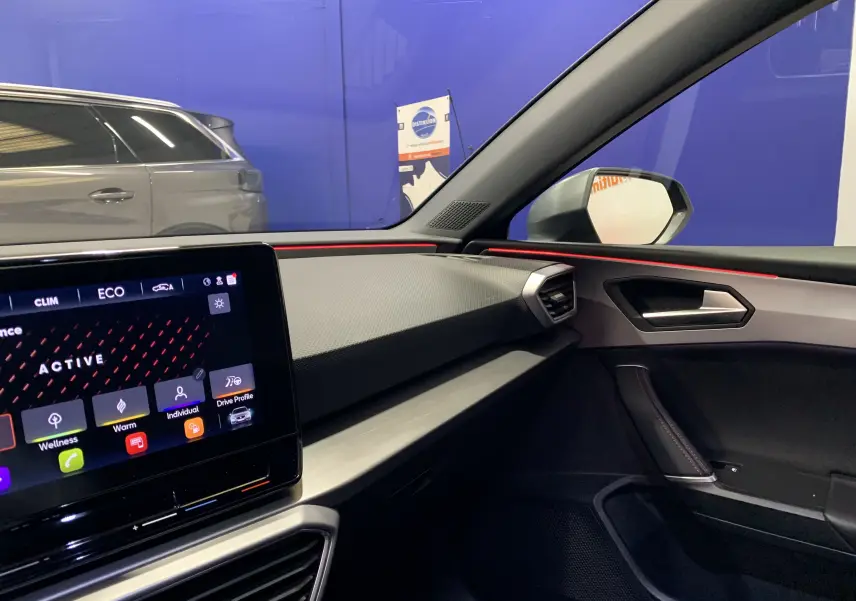 Intérieur côté passager du SEAT Leon gris 2020, tableau de bord moderne avec écran tactile et bandeau lumineux rouge.