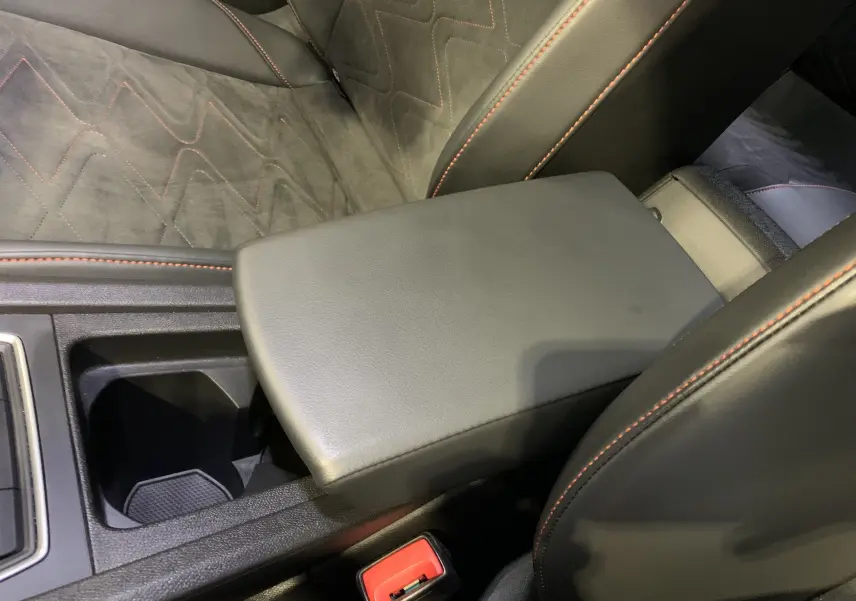 Gros plan sur l'accoudoir central noir et les sièges gris foncé avec surpiqûres orange dans la SEAT Leon E-HYBRID 2020.