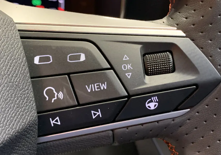 Détail des commandes noires sur le volant perforé de la SEAT LEON E-HYBRID 204 FR DSG6 gris, boutons fonctionnels éclairés.