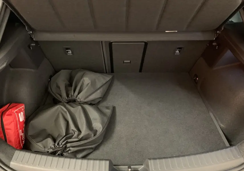 Coffre ouvert d'une SEAT LEON E-HYBRID gris 2020, vue intérieure montrant un rangement propre avec sacs et trousse de secours rouge.