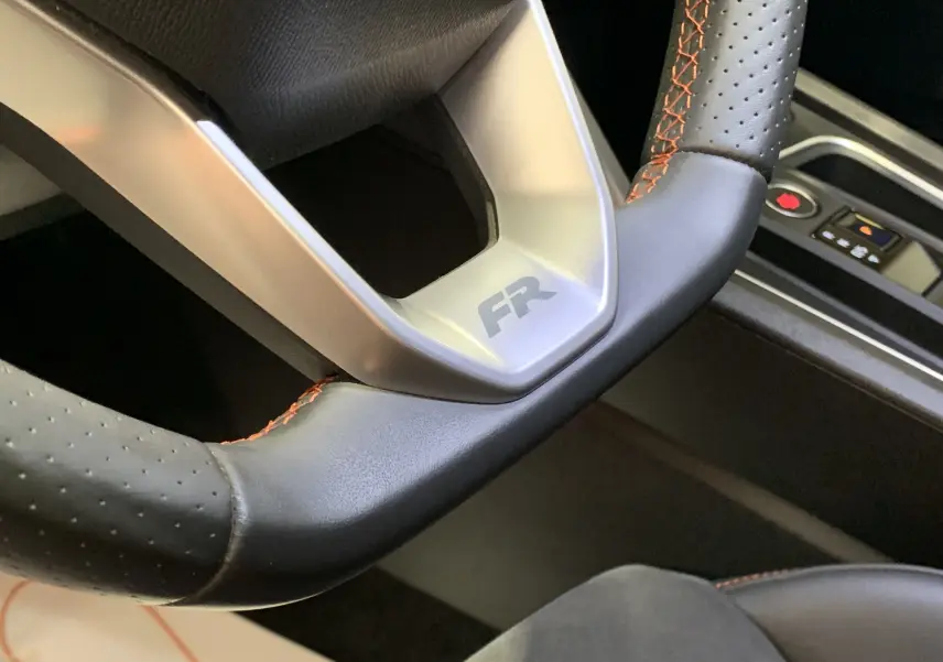 Gros plan sur le volant en cuir noir avec surpiqûres orange et logo FR de la SEAT LEON E-HYBRID 204 FR DSG6.