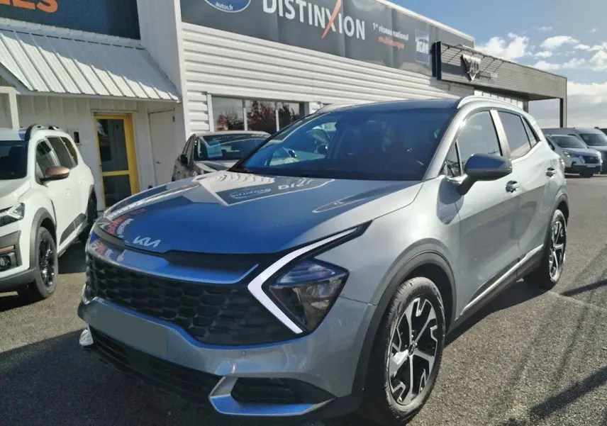 KIA Sportage gris perle en 3/4 avant droit, avec calandre noire distinctive et jantes bicolores.