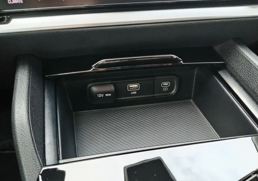 Gros plan sur la console centrale du Kia Sportage 2025, montrant les ports USB et prise 12V dans un intérieur noir.