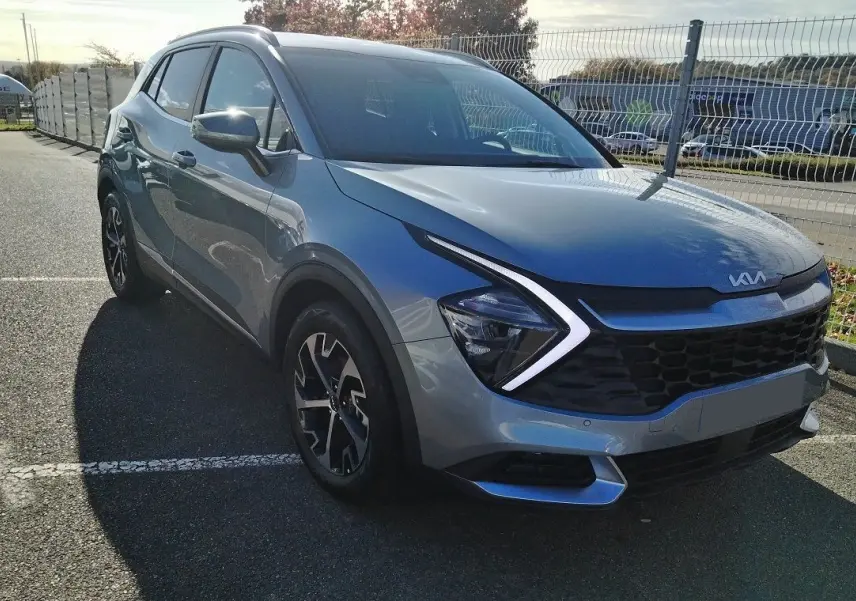 KIA Sportage gris perle en 3/4 avant droit, avec signature lumineuse en forme de flèche et calandre noire.