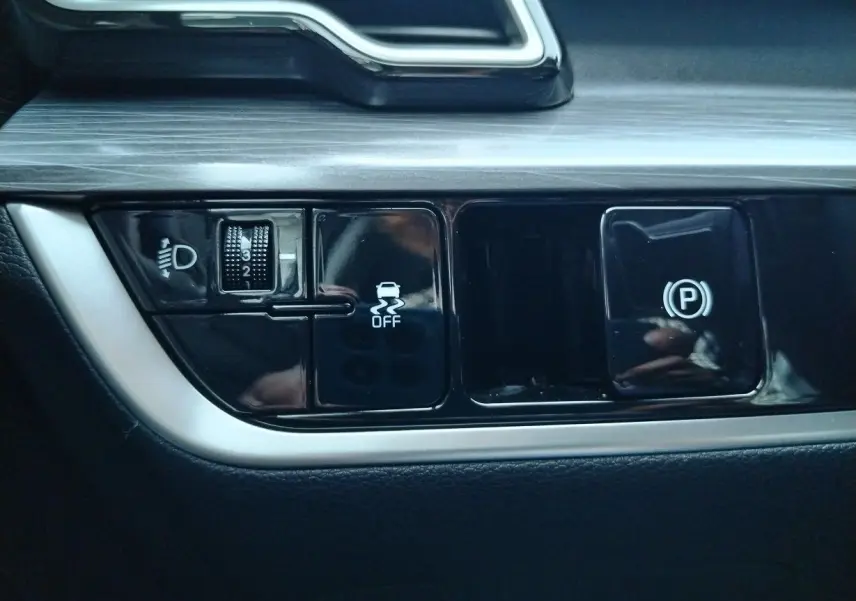 Gros plan sur les commandes noires du tableau de bord du Kia Sportage 2025, avec réglage des phares et frein de stationnement.