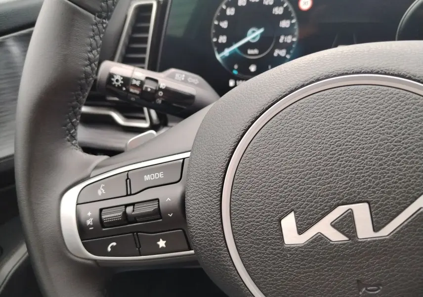 Gros plan sur le volant noir du Kia Sportage 2025 avec commandes intégrées et tableau de bord numérique en arrière-plan.