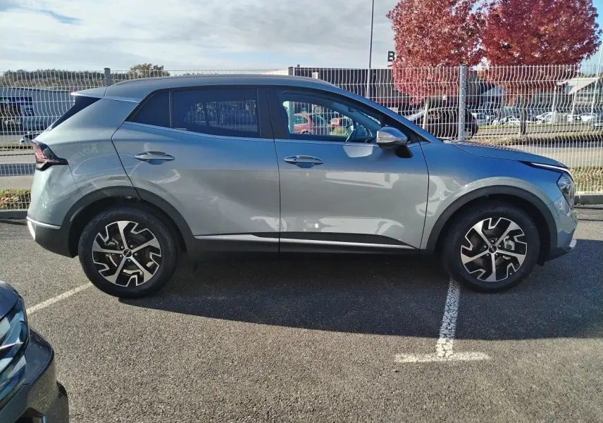 Vue de profil côté gauche du KIA Sportage gris perle 2025 avec jantes bi-ton et toit noir contrasté.