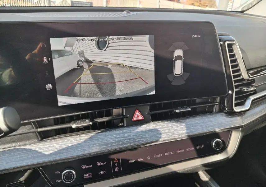 Écran central du Kia Sportage 2025 montrant la caméra de recul avec vue arrière et lignes de guidage jaunes et rouges.