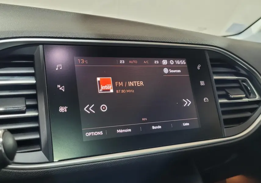 Écran tactile central allumé affichant la radio FM dans l'habitacle d'une Peugeot 308 gris foncé de 2020.