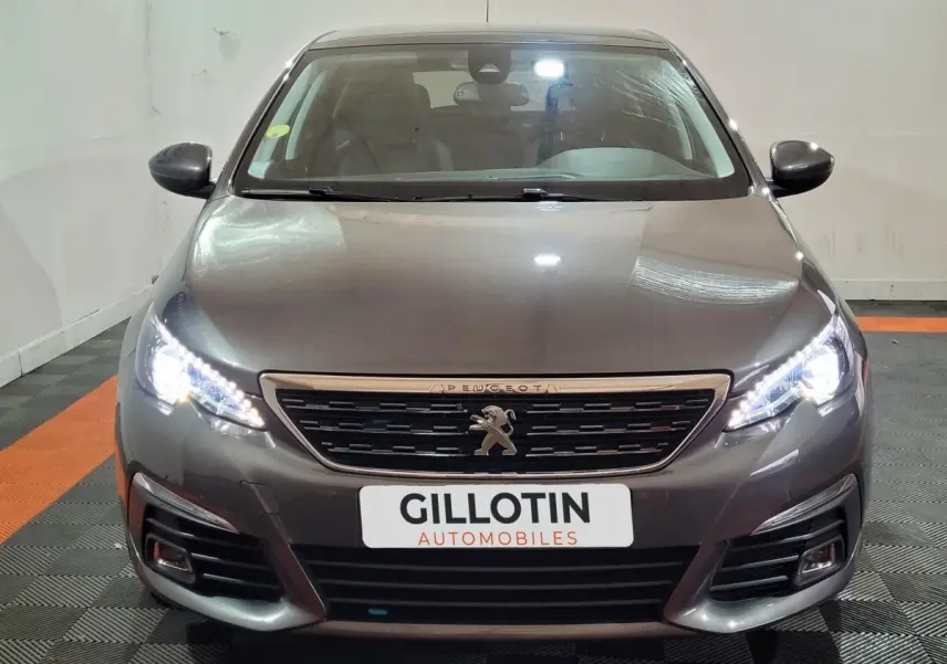 Vue frontale d'une Peugeot 308 gris foncé avec phares LED allumés et calandre distinctive au lion Peugeot.
