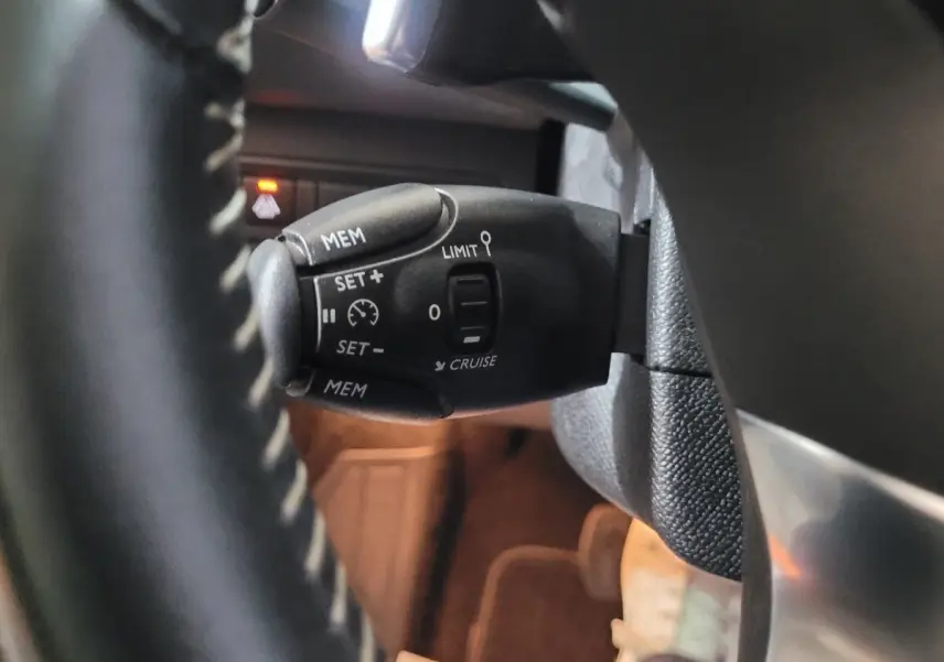 Gros plan sur la commande de régulateur de vitesse au volant cuir d'une Peugeot 308 gris foncé de 2020.