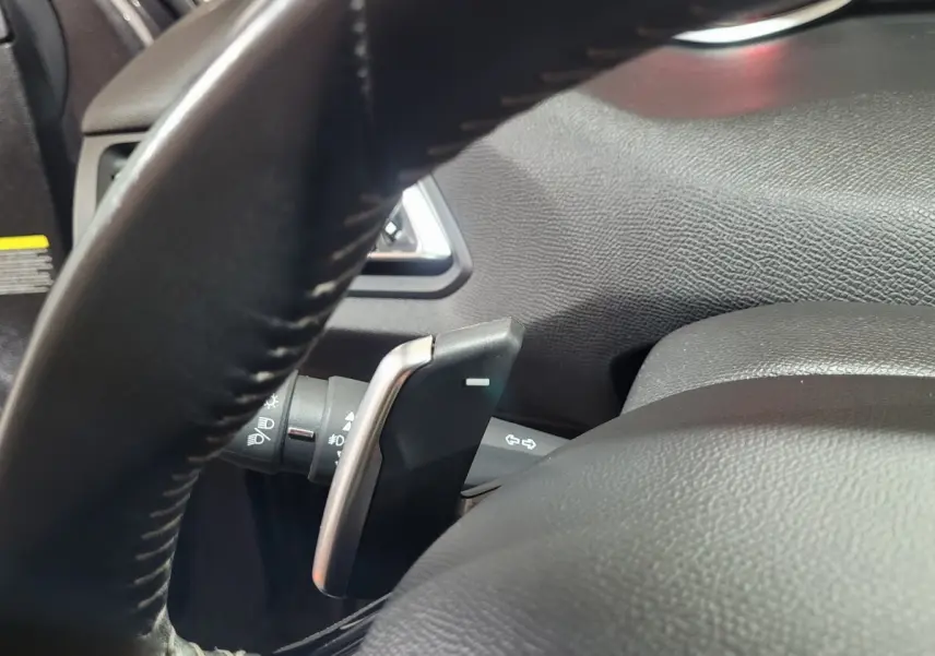 Gros plan sur la palette de changement de vitesse derrière le volant cuir noir d'une Peugeot 308 gris foncé de 2020.