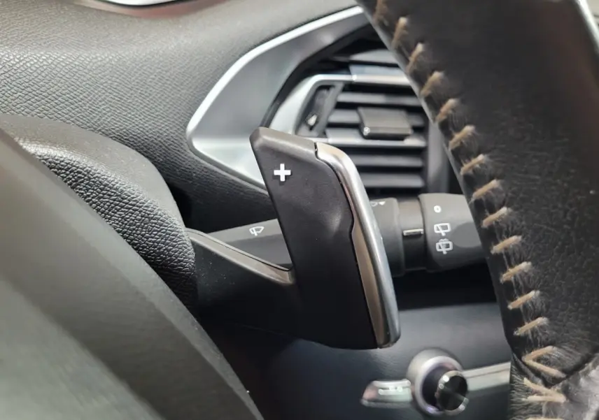Gros plan sur la palette de changement de vitesse + au volant cuir de la Peugeot 308 gris foncé, intérieur noir.