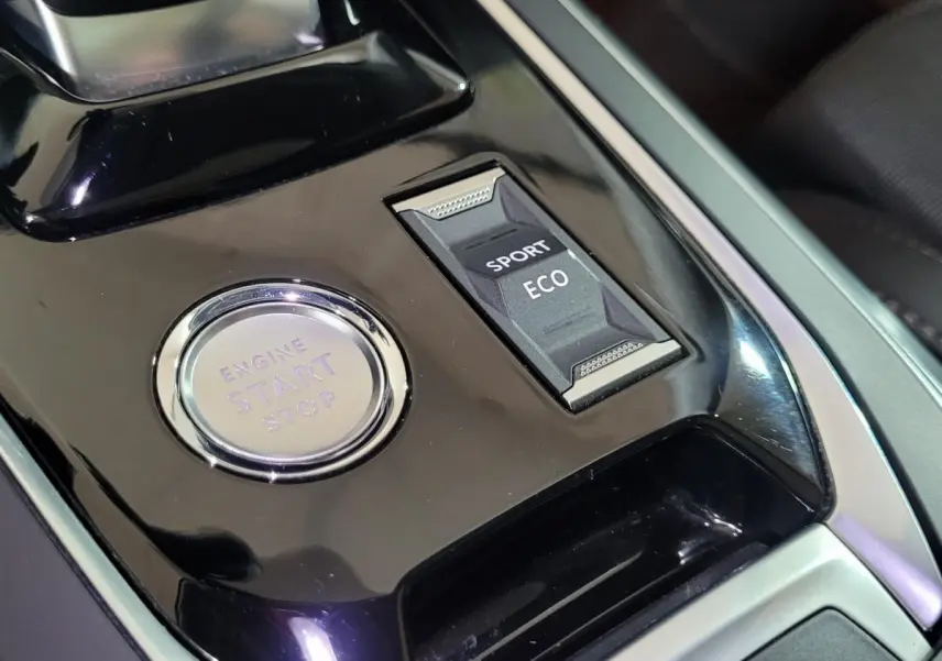 Vue rapprochée de la console centrale noire de la Peugeot 308 avec bouton démarrage et sélecteur modes Sport/Eco.