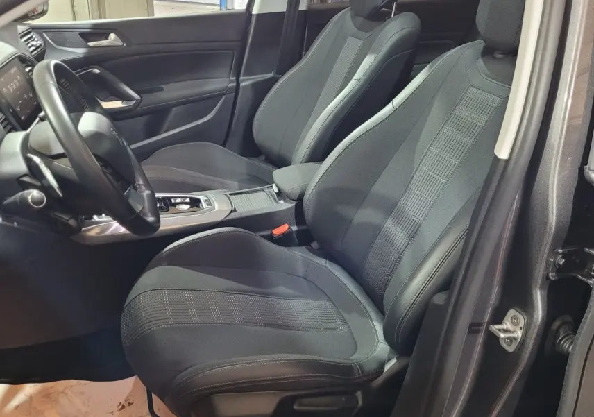 Vue intérieure côté conducteur de la Peugeot 308 gris foncé, mettant en valeur les sièges avant et le volant cuir multifonctions.