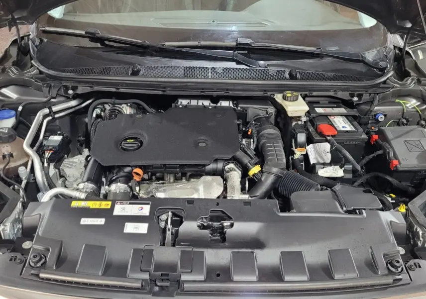 Vue rapprochée du compartiment moteur de la Peugeot 308 gris foncé, montrant les composants et la batterie.