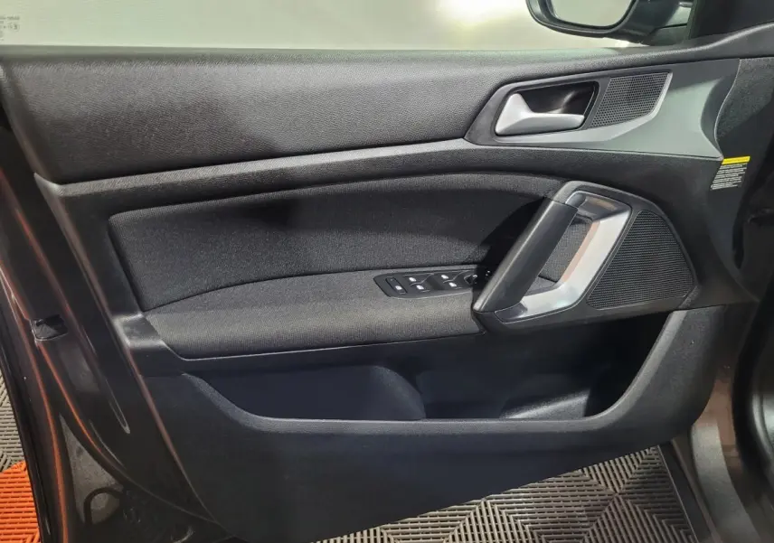 Vue rapprochée de la porte côté gauche d'une Peugeot 308 gris foncé, avec commandes électriques et poignée argentée.