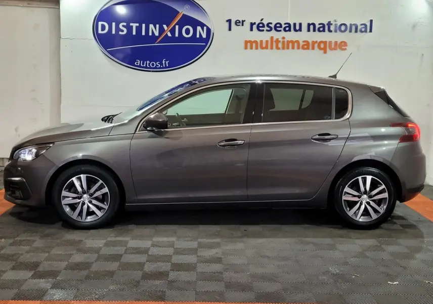 Profil côté gauche d'une Peugeot 308 gris foncé 2020 garée en intérieur sur sol damier, avec jantes alliage visibles.