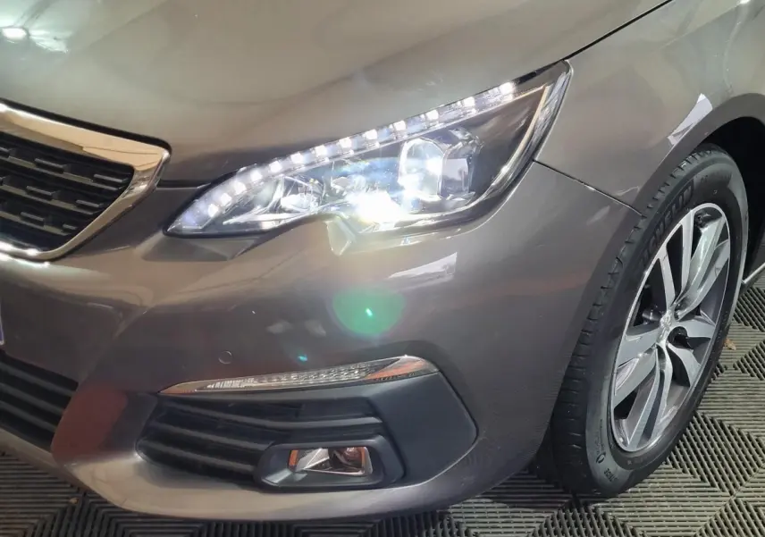 Gros plan sur l'avant droit d'une Peugeot 308 gris foncé, mettant en valeur le phare LED et la roue alliage.
