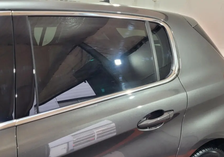 Vue latérale côté droit de la Peugeot 308 gris foncé avec poignées de porte et contours de vitres chromés.