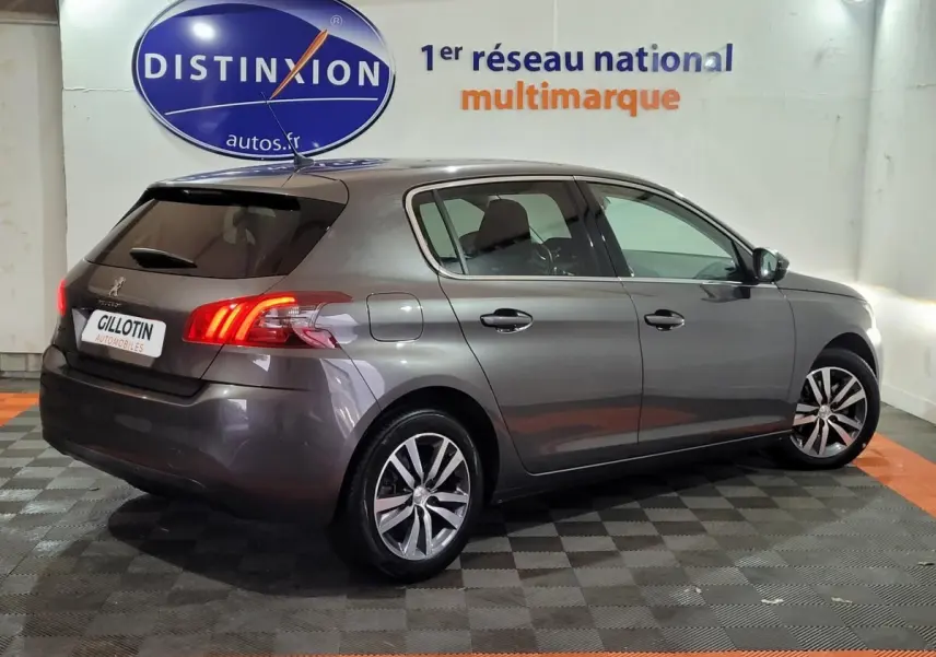 Peugeot 308 gris foncé vue de profil côté droit, feux arrière allumés dans un garage multimarque.