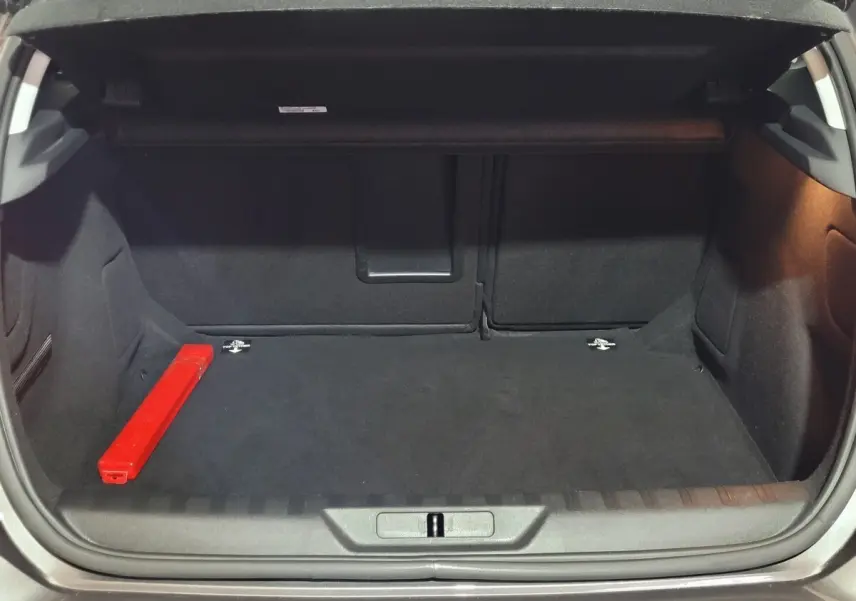 Coffre ouvert d'une Peugeot 308 gris foncé, montrant l'espace de chargement avec un triangle de signalisation rouge à gauche.
