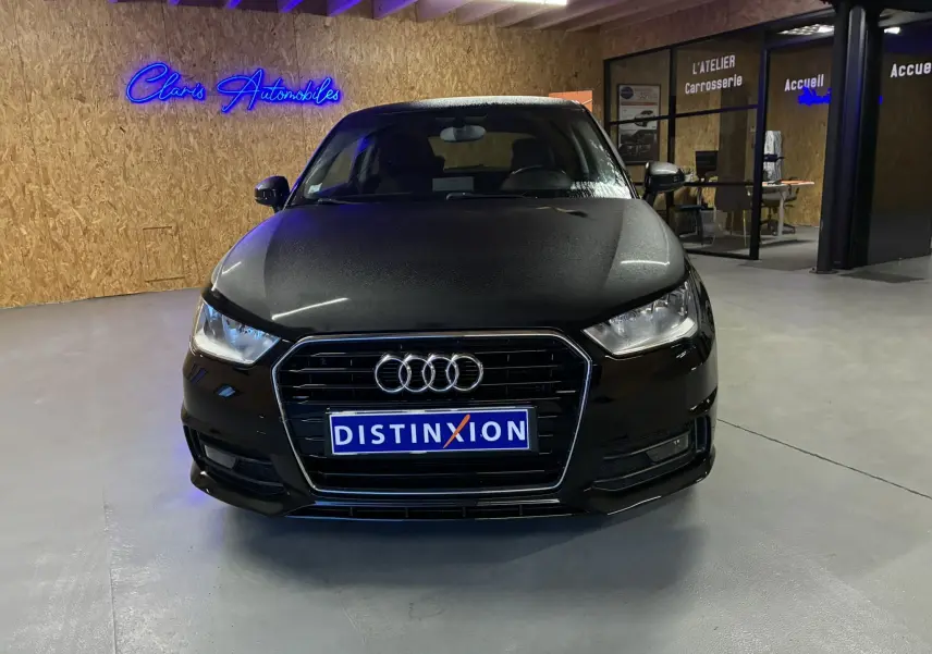 Vue de face d'une Audi A1 noire 2016 avec calandre chromée et logo quatre anneaux, dans un showroom intérieur.
