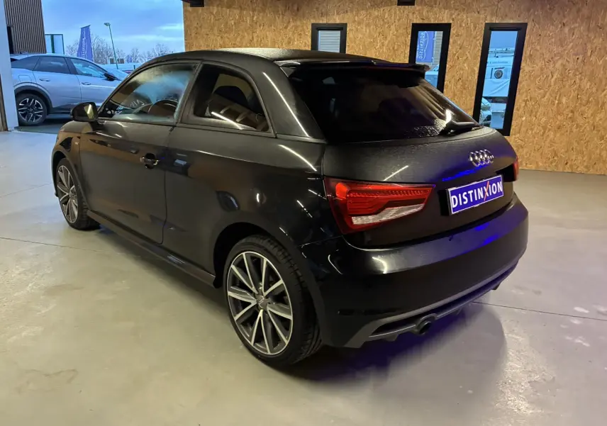 Audi A1 noir en vue 3/4 arrière droit, avec jantes alliage et toit contrasté dans un garage intérieur.