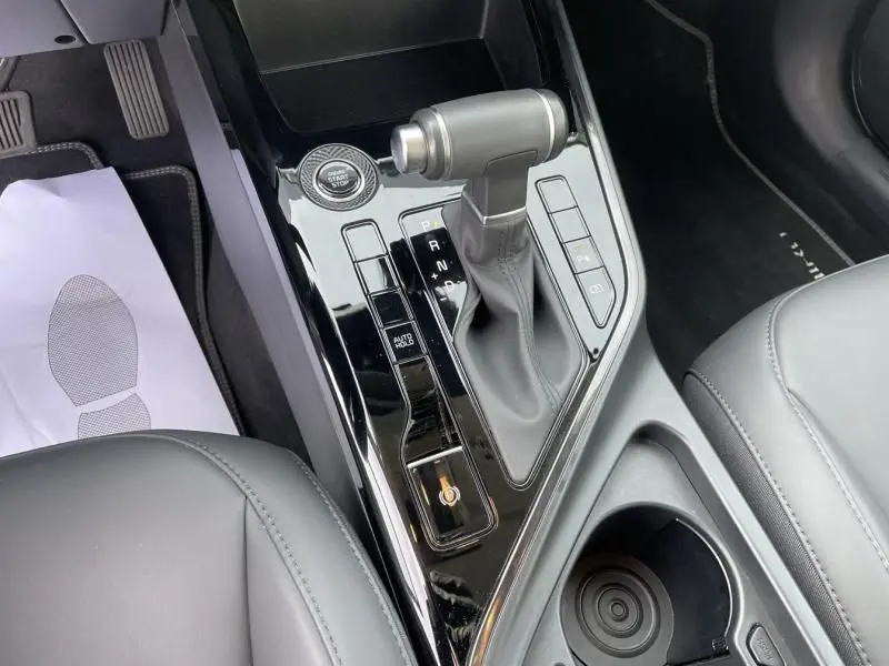 Gros plan sur la console centrale du KIA Niro 2024, boîte auto et bouton start/stop, intérieur cuir gris.