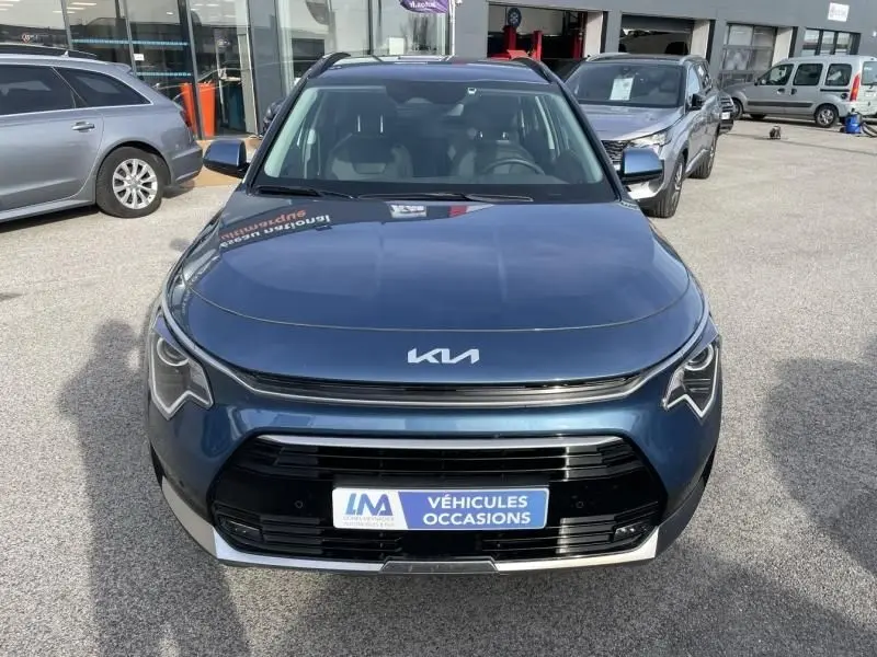 Vue avant d’un KIA Niro 2024 bleu métal avec calandre noire et logo KIA moderne, stationné en extérieur.