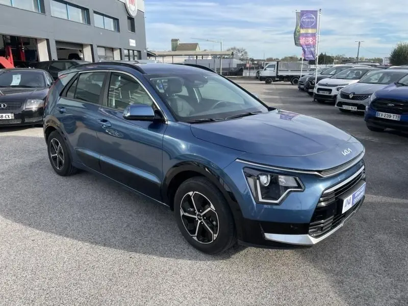 KIA Niro 2024 bleu métal en vue 3/4 avant droit, avec signature lumineuse distinctive et jantes noires.