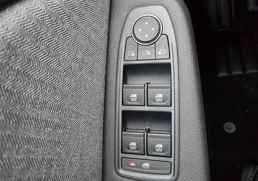 Gros plan sur les commandes des vitres électriques côté gauche avec tissu gris mélangé à chevrons dans une Renault Clio 2025.