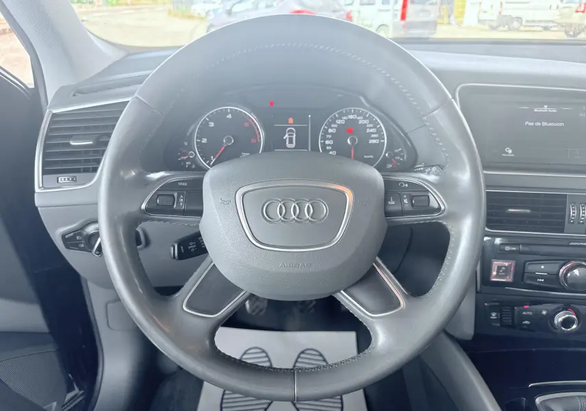 Vue intérieure centrée sur le volant noir d'un Audi Q5 2014, avec tableau de bord et console centrale visibles.