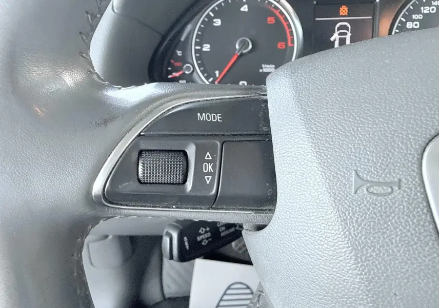 Gros plan sur le volant noir de l'Audi Q5 2014, montrant les commandes de mode et le compteur partiel en arrière-plan.