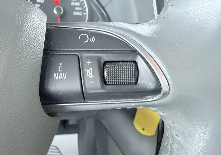 Gros plan sur les commandes de navigation et volume au volant d’un Audi Q5 noir, tableau de bord partiellement visible.