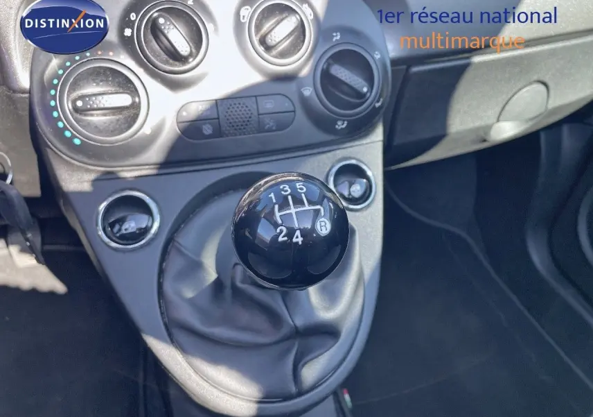 Gros plan sur le levier de vitesses manuel noir dans l'habitacle d'une Fiat 500C grise, avec commandes de climatisation visibles.