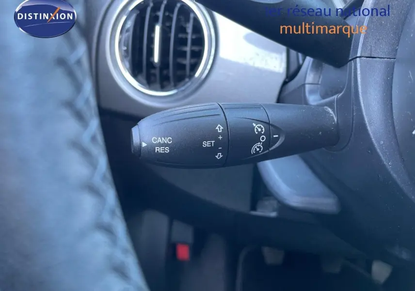 Gros plan sur la commande de régulateur de vitesse à gauche du volant dans l'habitacle d'une Fiat 500C grise.