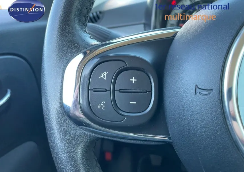 Gros plan sur les commandes de volume et de son du volant d'une FIAT 500C grise électroclash, intérieur visible en arrière-plan.