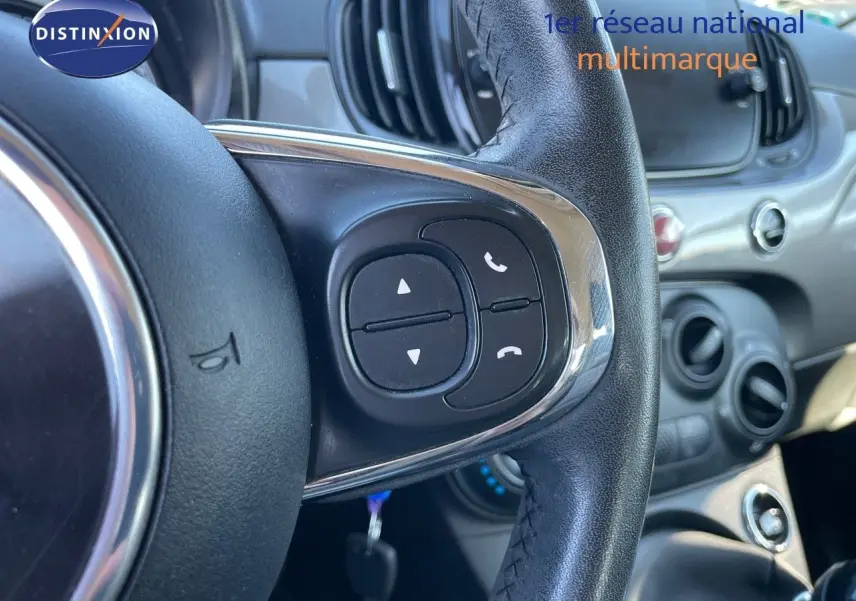 Gros plan sur le volant noir de la Fiat 500C 2019 avec commandes intégrées, tableau de bord gris métallisé en arrière-plan.