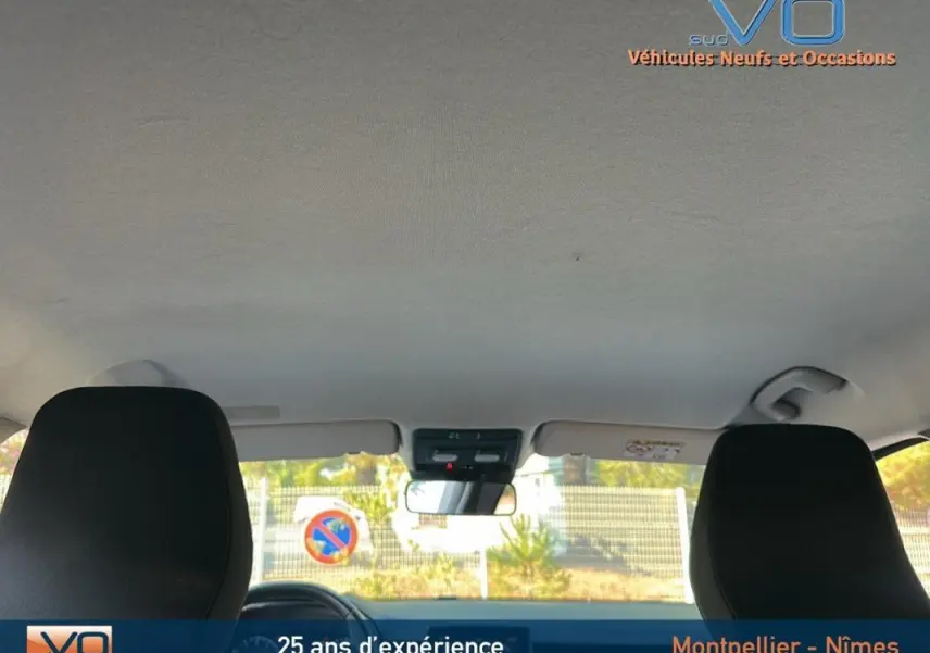 Vue intérieure avant de la Renault Clio 2023, sièges noirs et pare-brise avec rétroviseur central visible.