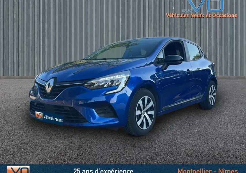 Renault Clio V TCe 90 Equilibre bleu foncé vue 3/4 avant droit sur sol gris devant un mur métallique.