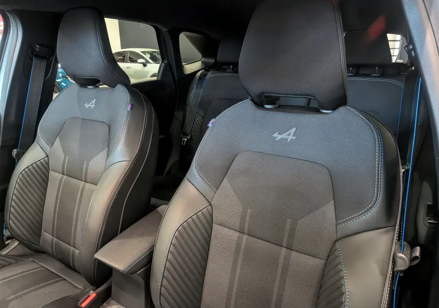 Vue rapprochée des sièges avant noirs avec surpiqûres bleues et logo Alpine sur le Renault Symbioz hybride 2026.