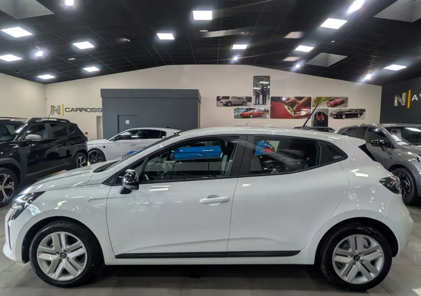 Profil latéral droit d'une Renault Clio V blanc glacier en showroom, avec jantes alliage et rétroviseurs noirs.
