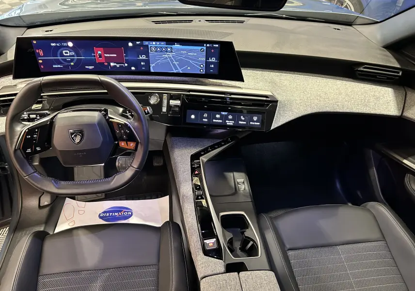 Vue intérieure du tableau de bord et volant du Peugeot 3008 Hybrid 2024 avec finition tissu et écran panoramique i-Cockpit.